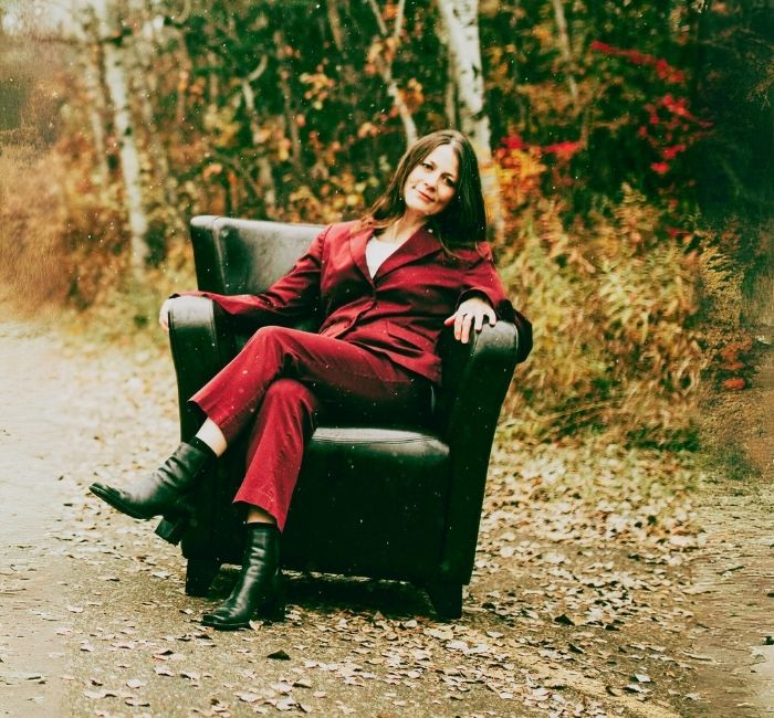 A dark haired woman sitting on a brown leather chair on a paved trail in autumn.