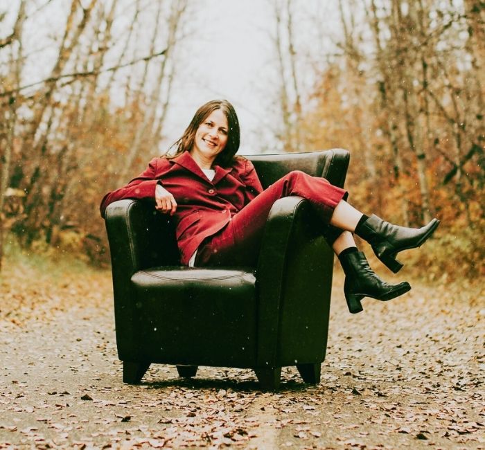 A dark haired woman sitting on a brown leather chair on a paved trail in autumn.
