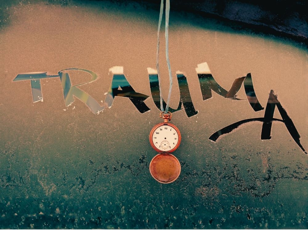 1000 x 750 A fogged up window with the handwritten word "trauma" along with a dangling timepiece reflecting the severity and often prolonged nature of trauma.