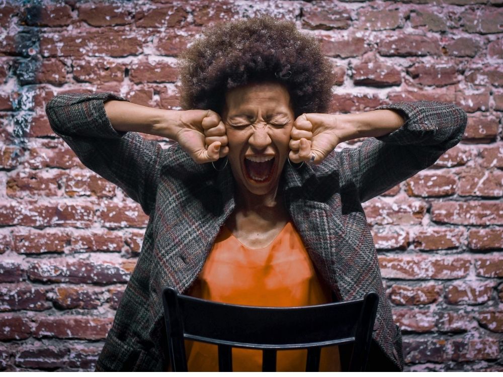 An distraught woman sitting on a back chair against a red brick wall.